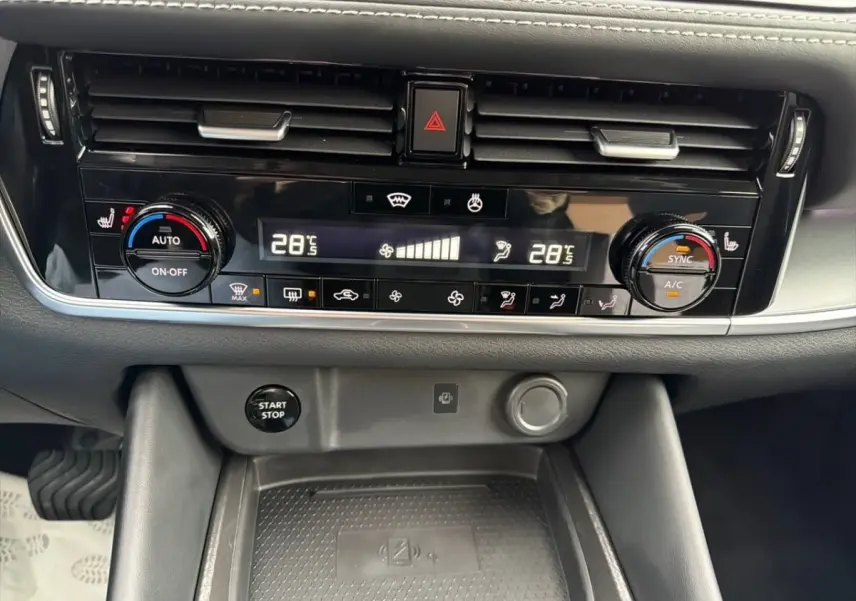 Vue rapprochée du tableau de bord noir du Nissan Qashqai 2025, avec commandes climatisation et bouton démarrage visible.