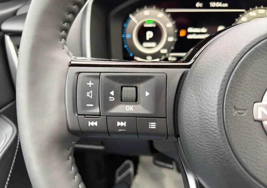 Gros plan sur les commandes gauche du volant cuir noir du Nissan Qashqai 2025 avec tableau de bord numérique en arrière-plan.