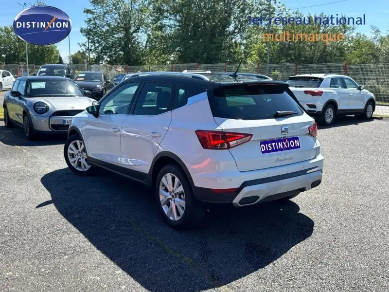 Vue 3/4 arrière droite d'une SEAT Arona 2025 blanc Nevada avec toit noir Minuit et jantes alu sur parking.