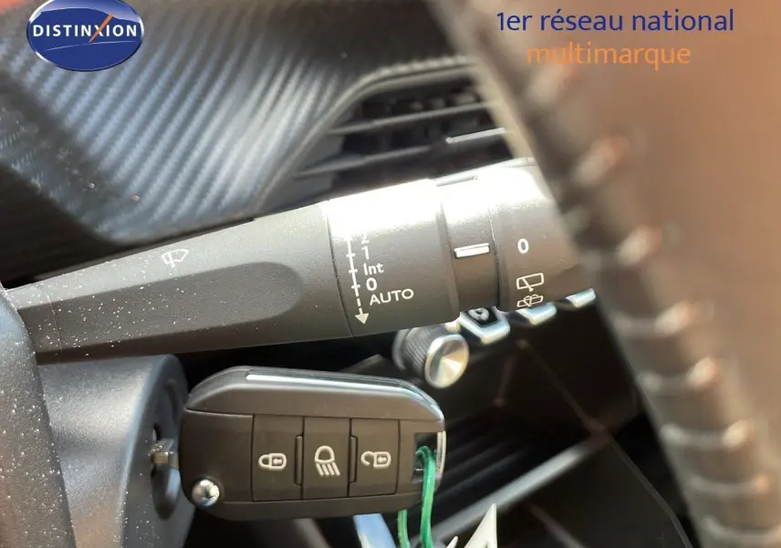 Gros plan sur la clé de contact insérée dans une Peugeot 2008 2024, avec commande d'essuie-glace visible derrière le volant.