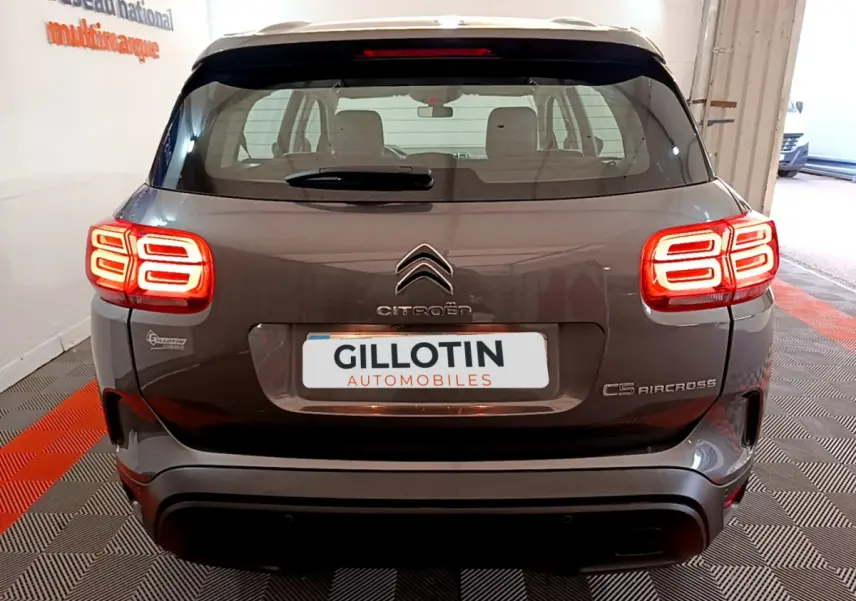 Vue arrière d'un Citroën C5 Aircross gris foncé avec feux arrière LED distinctifs allumés en intérieur showroom.