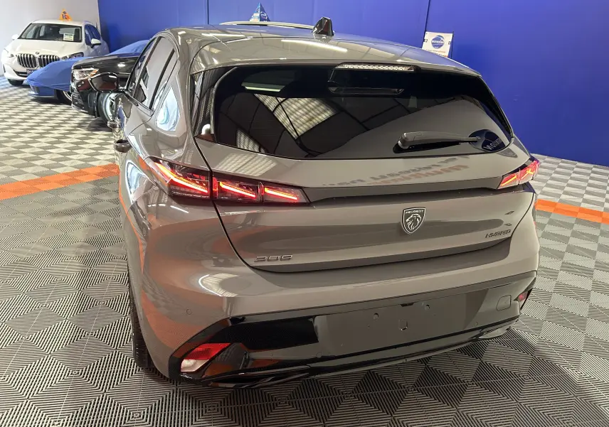 Vue 3/4 arrière droite d'une Peugeot 308 III Ph.2 Hybrid 145 GT gris Selenium avec feux arrière LED allumés.