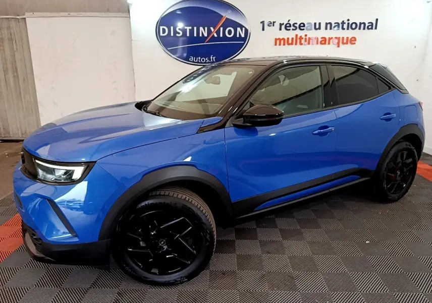 Vue 3/4 avant droite d’un Opel Mokka 2024 bleu avec toit noir et jantes noires dans un showroom.