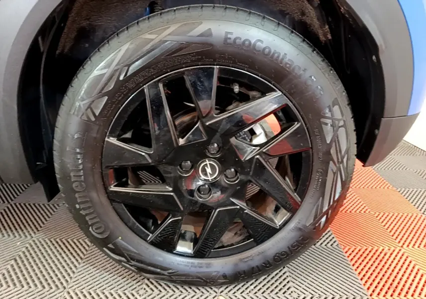 Gros plan sur la roue avant droite noire brillante de l’Opel Mokka bleu, avec logo Opel au centre.