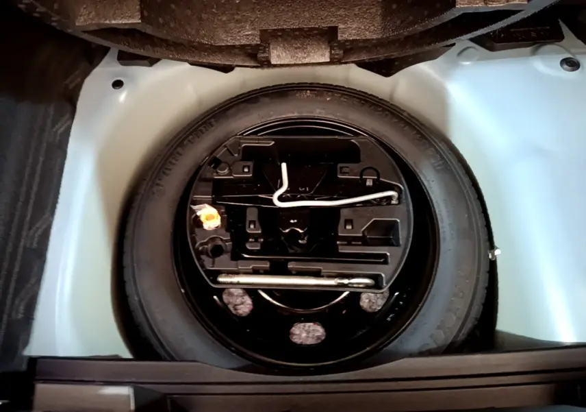 Vue plongeante sur la roue de secours noire et ses outils dans le coffre clair d’un Opel Mokka 2024.