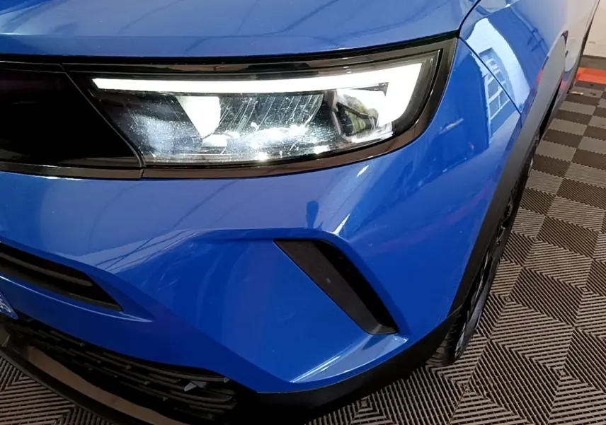 Gros plan sur l'avant droit bleu de l'Opel Mokka 2024, mettant en valeur le phare LED et la calandre noire.