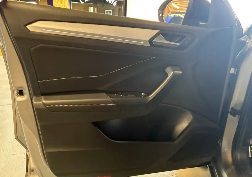 Vue intérieure de la porte avant gauche du Volkswagen T-Roc gris clair, avec garniture noire et surpiqûres claires.