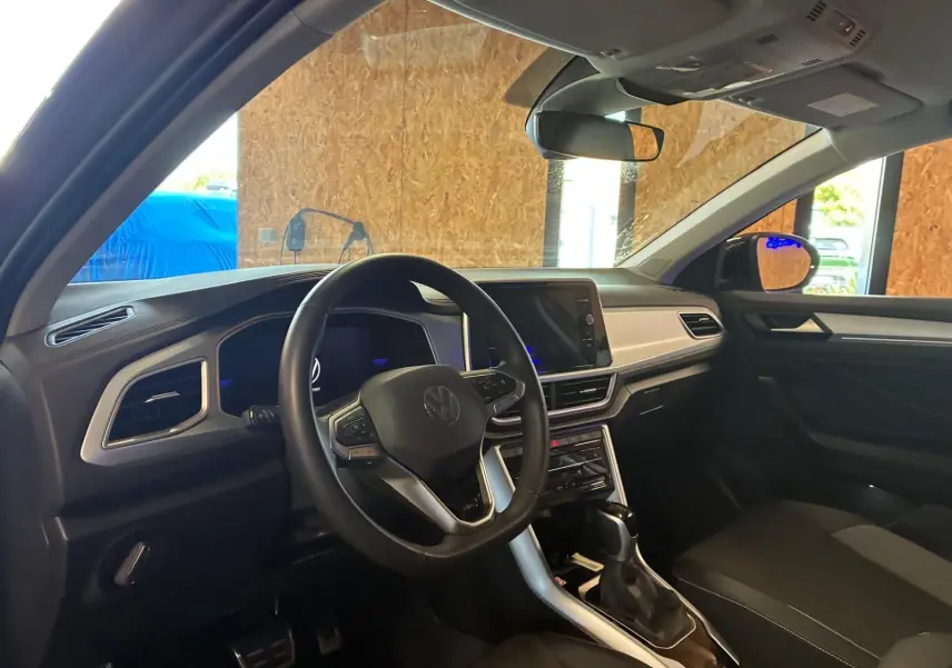 Vue intérieure côté conducteur du Volkswagen T-Roc gris clair 2025, avec volant multifonction et écran tactile central.