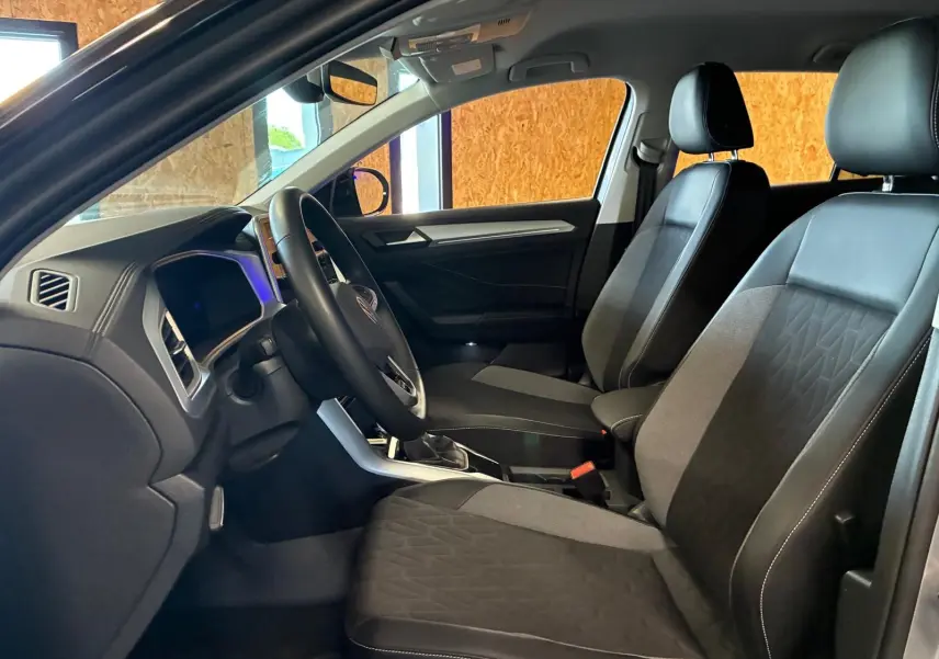 Vue intérieure côté conducteur du Volkswagen T-Roc 2025, montrant les sièges tissu noir et la planche de bord moderne.