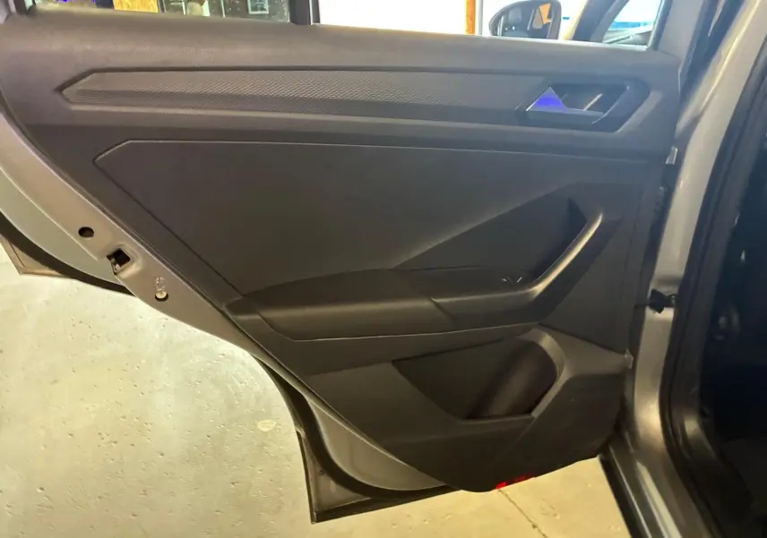 Vue intérieure de la porte arrière droite du Volkswagen T-Roc gris clair, montrant le panneau de porte noir avec poignée intégrée.