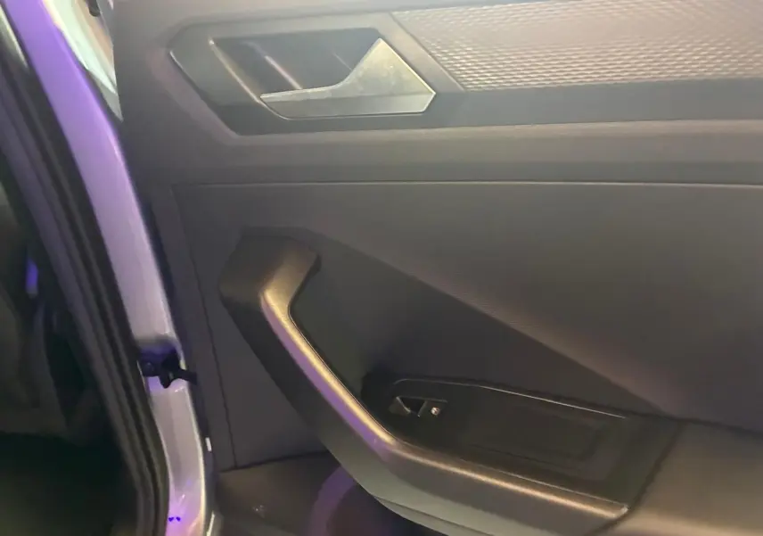 Gros plan sur la porte intérieure côté gauche du Volkswagen T-Roc gris clair, mettant en valeur la poignée et les commandes.