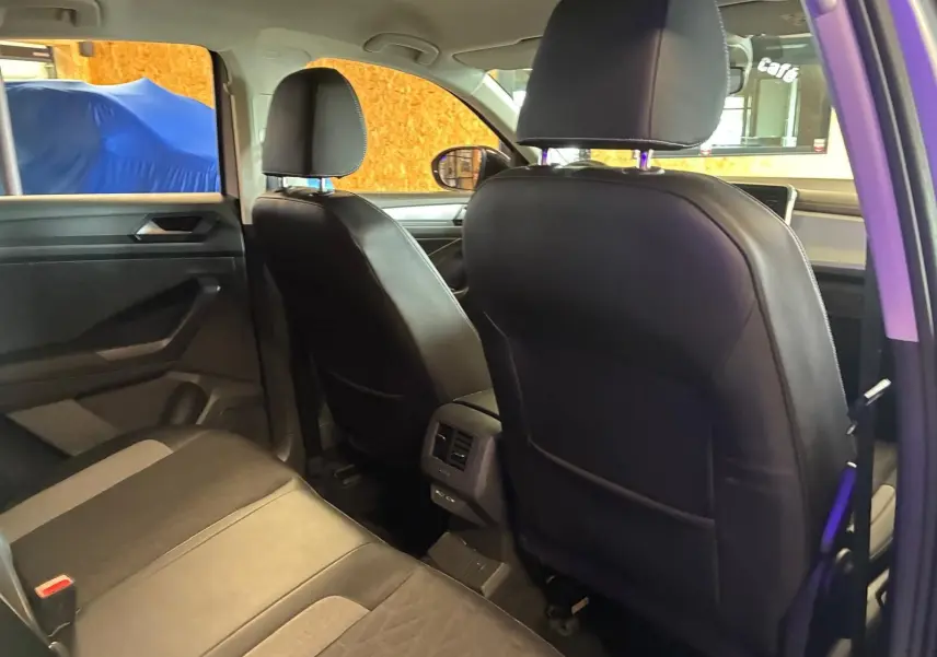 Vue intérieure arrière du Volkswagen T-Roc gris clair 2025, sièges en tissu noir avec détails gris et aérateurs centraux.