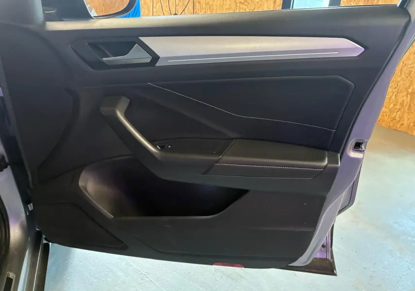 Vue intérieure de la porte avant gauche du Volkswagen T-Roc gris clair, avec garniture noire et surpiqûres blanches.