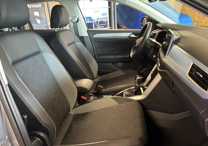 Vue intérieure côté gauche du Volkswagen T-Roc 2025, sièges tissu gris foncé avec motifs géométriques et tableau de bord moderne.