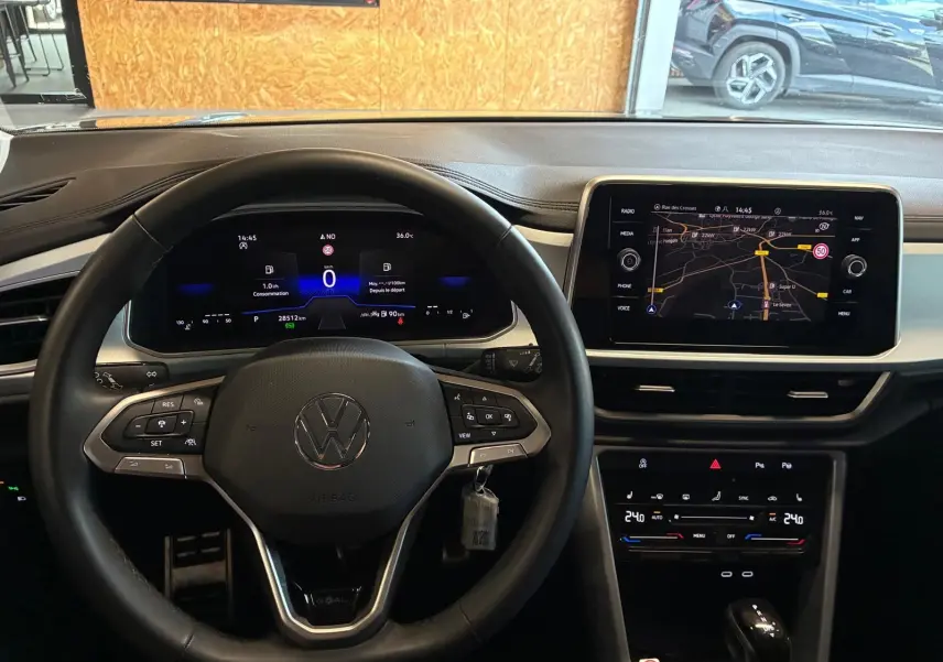 Vue intérieure centrée sur le volant noir et le tableau de bord numérique du Volkswagen T-Roc 2025 gris clair.