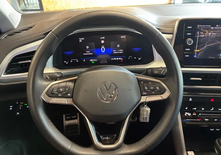 Vue centrée sur le volant du Volkswagen T-Roc 2025, tableau de bord numérique et écran tactile de navigation visibles.