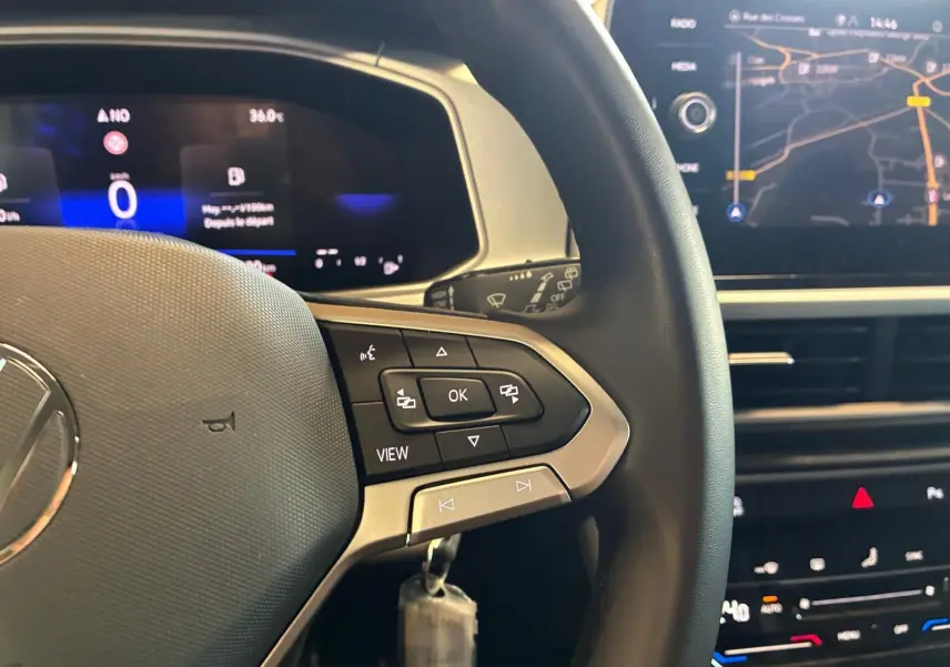 Vue rapprochée du volant noir du Volkswagen T-Roc 2025 avec commandes intégrées et écran numérique en arrière-plan.