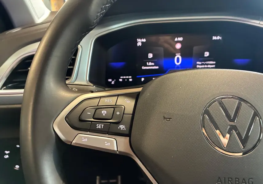 Vue rapprochée du volant noir de Volkswagen T-Roc 2025 avec commandes intégrées et tableau de bord numérique allumé.