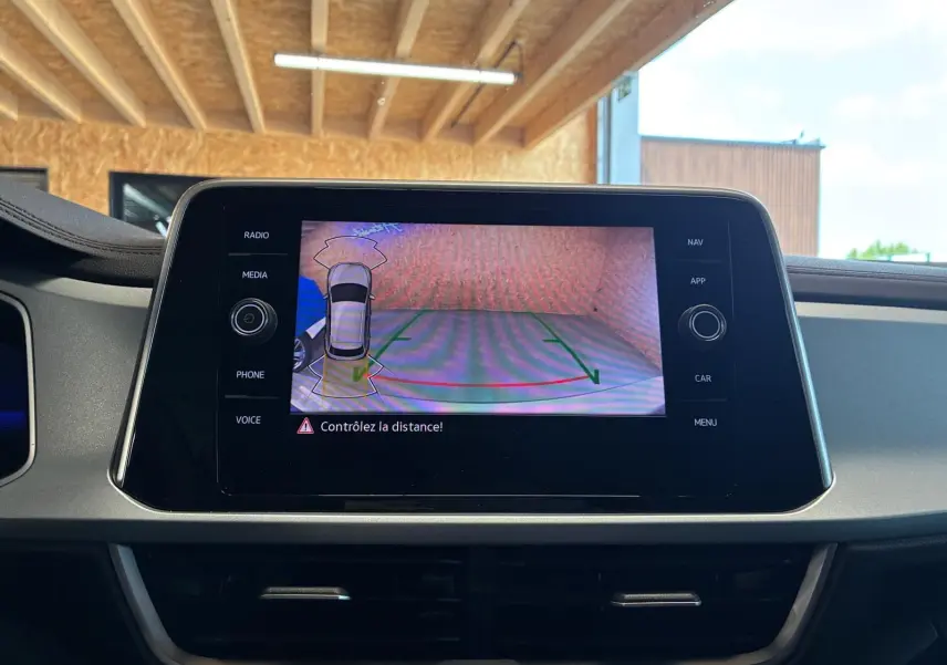 Écran central du Volkswagen T-Roc 2025 montrant la caméra de recul avec alertes de distance, intérieur noir.