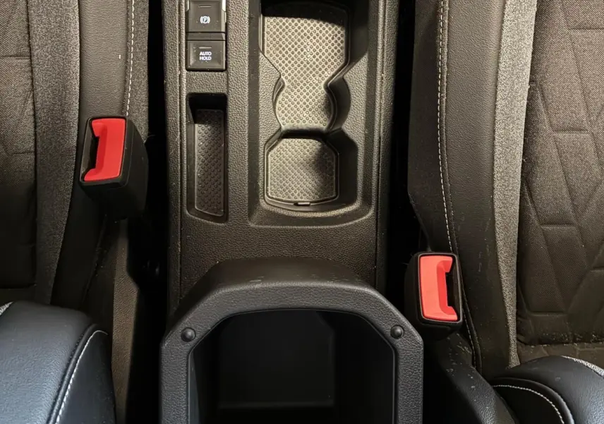Vue plongeante sur la console centrale noire du Volkswagen T-Roc 2025 avec porte-gobelets et boutons de frein à main électronique.