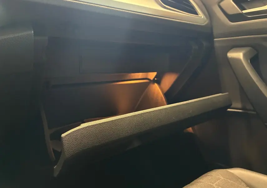 Gros plan intérieur sur la boîte à gants ouverte du Volkswagen T-Roc 2025, éclairage intérieur chaud visible.