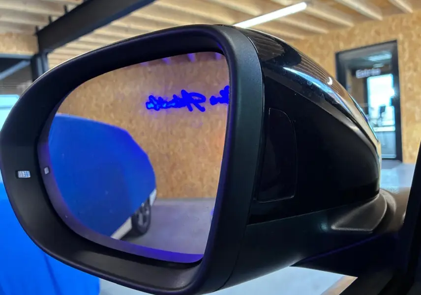 Rétroviseur extérieur côté gauche noir du Volkswagen T-Roc gris clair 2025, vue rapprochée en intérieur.