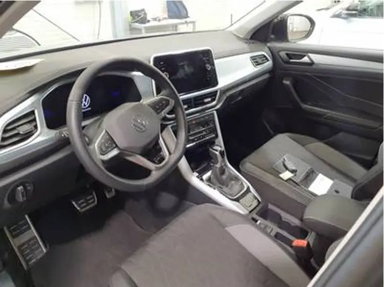 Vue intérieure côté conducteur du Volkswagen T-Roc 2025, avec tableau de bord moderne et sellerie tissu gris.