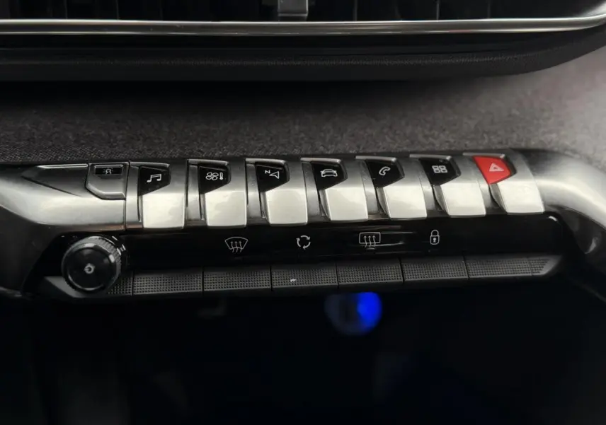 Gros plan sur les commandes centrales métalliques et noires du tableau de bord du Peugeot 5008 GT Line bleu foncé.