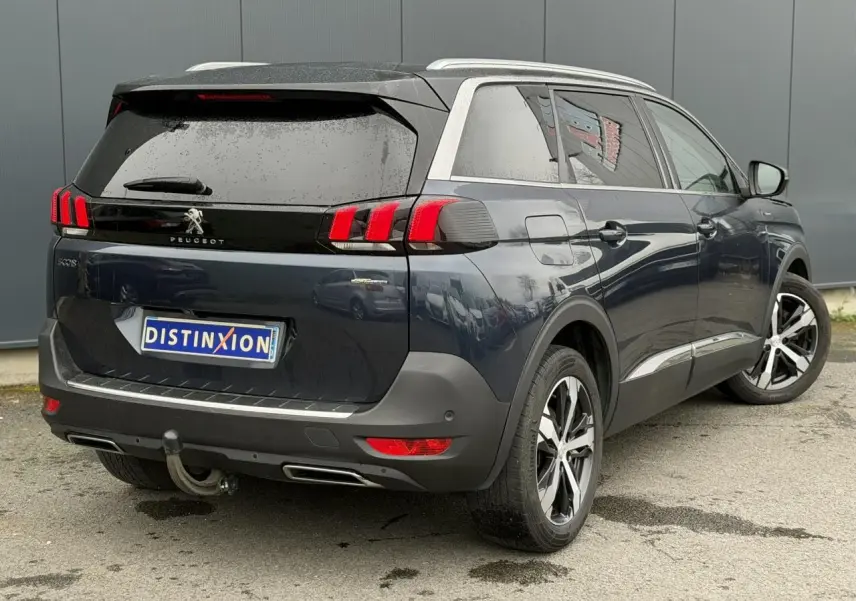 Vue 3/4 arrière droite d’un Peugeot 5008 bleu foncé avec toit noir et jantes alliage bi-ton.