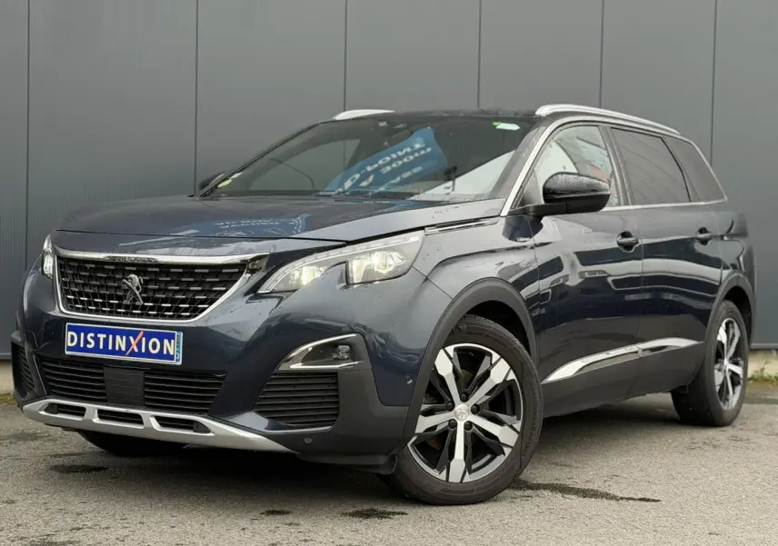Vue 3/4 avant droit d’un Peugeot 5008 bleu foncé avec jantes alliage bi-ton et barres de toit argentées.