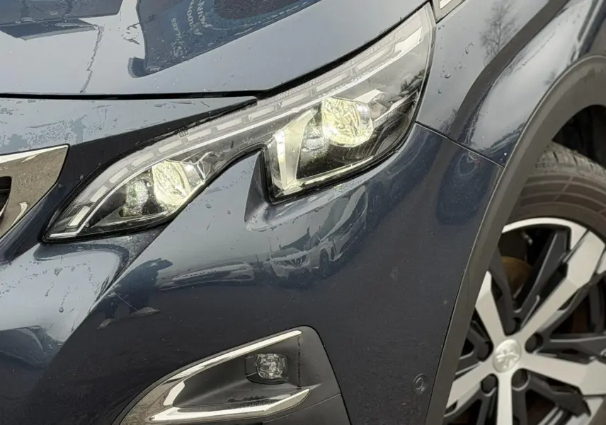 Gros plan sur l'avant droit du Peugeot 5008 bleu foncé, mettant en valeur le phare LED et la jante alliage bi-ton.