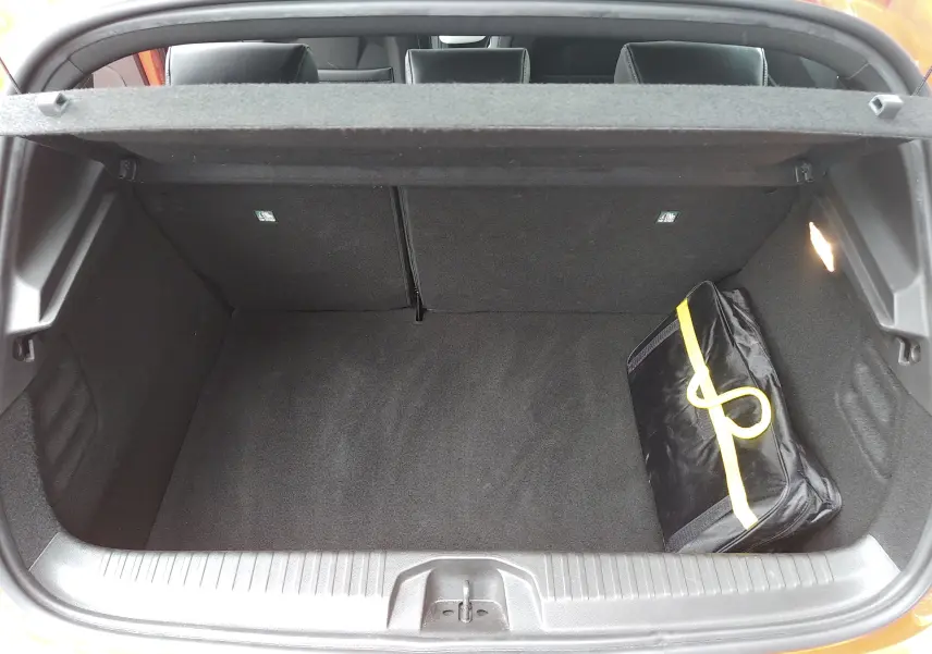 Coffre ouvert vu de l'arrière d'une Renault Clio V orange, avec un sac noir à bande jaune à l'intérieur.