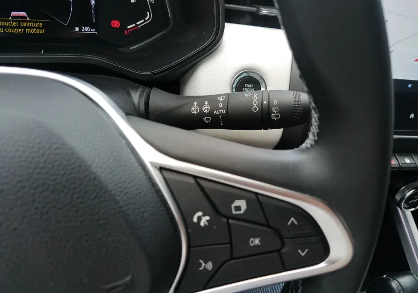 Gros plan sur le volant et la commande d’essuie-glace de la Renault Clio V E-TECH orange, intérieur noir et blanc.