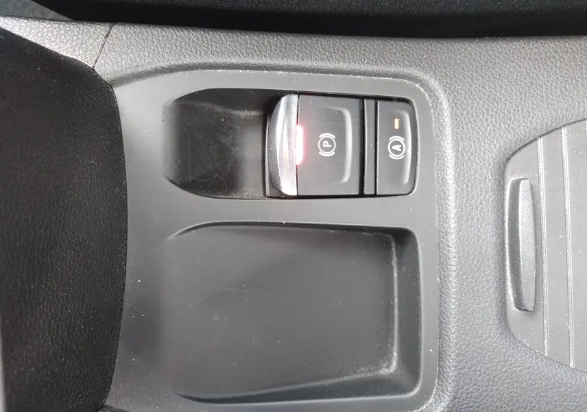 Gros plan sur les commandes de frein à main électrique et auto hold dans le console centrale noire d’une Renault Clio V orange.