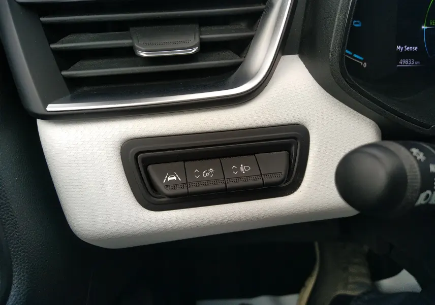 Détail intérieur du tableau de bord blanc texturé de la Renault Clio V E-TECH, avec boutons de réglage d'assistance et éclairage.