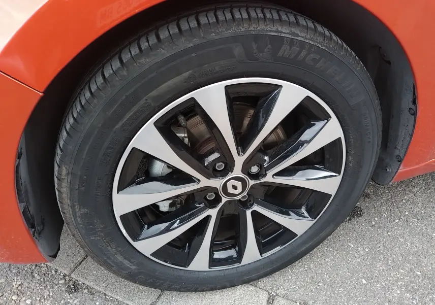 Gros plan sur la roue avant gauche orange d'une Renault Clio V E-TECH avec jante alliage bicolore et logo Renault central.