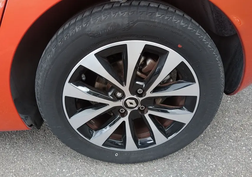 Gros plan sur la roue avant droite orange d'une Renault Clio V E-TECH avec jante alliage bicolore et logo Renault central.