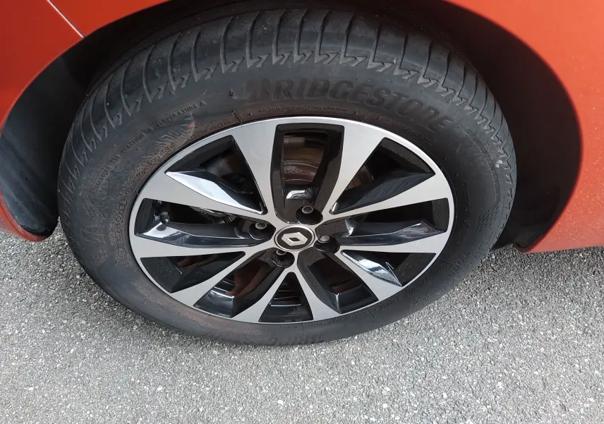 Gros plan sur la roue avant droite orange d'une Renault Clio V E-TECH 140ch avec jante alliage noire et argent.