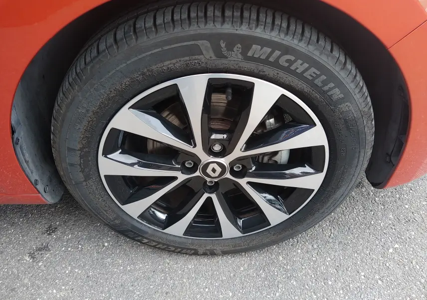 Gros plan sur la roue avant gauche orange d’une Renault Clio V E-TECH avec jante alliage noire et argentée.