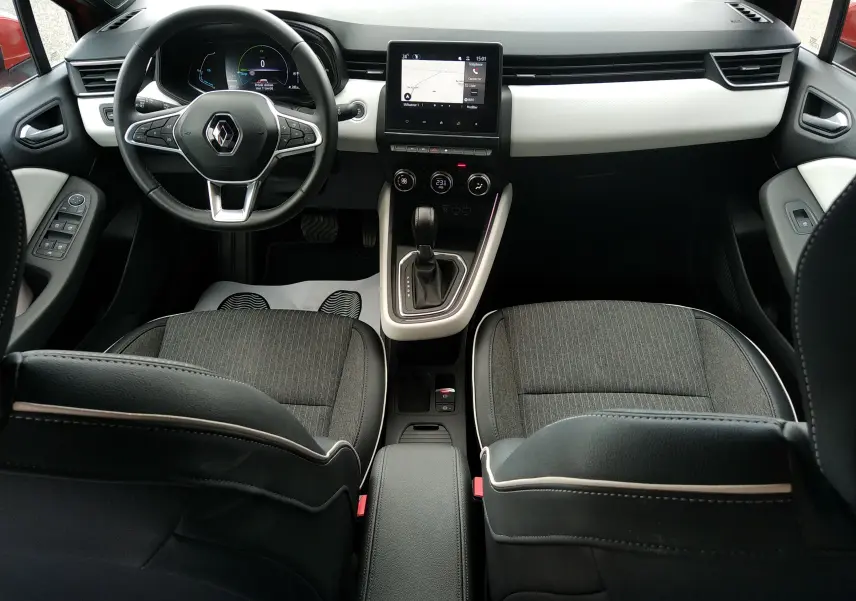 Vue intérieure avant de la Renault Clio V E-TECH 140ch, avec tableau de bord noir et blanc, écran tactile central et sièges tissu noir.