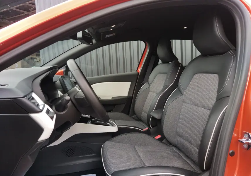Vue intérieure côté conducteur de la Renault Clio V E-TECH orange, sièges tissu et cuir gris avec surpiqûres blanches.
