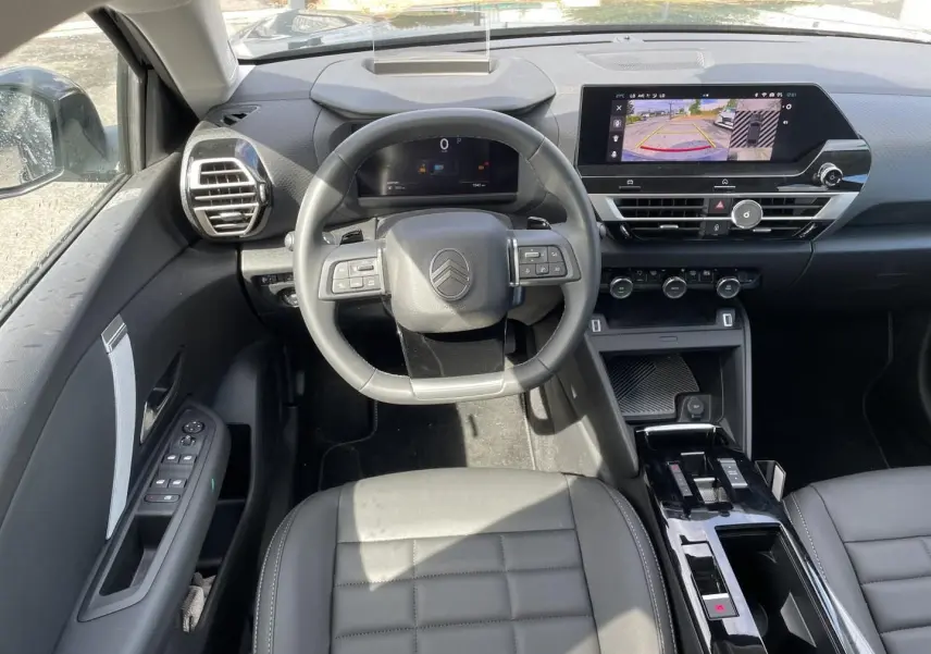 Vue intérieure avant centrée sur le volant cuir et l'écran tactile affichant la caméra de recul du Citroën C4 X noir.