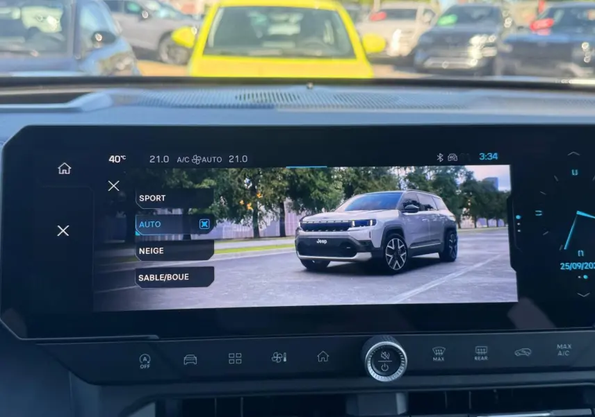 Écran tactile intérieur montrant un Jeep Compass gris en 3/4 avant sur route urbaine, avec arbres en arrière-plan.