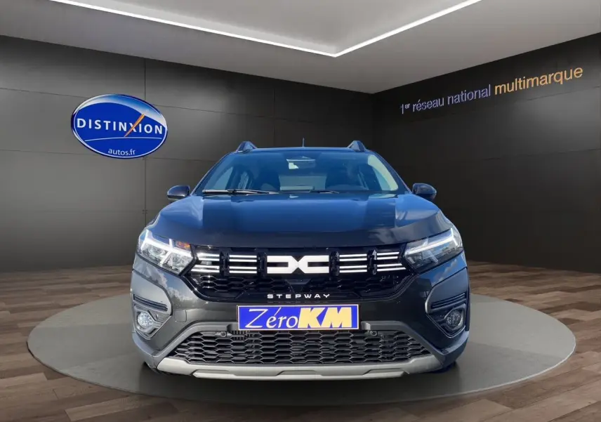 Vue frontale d'une Dacia Sandero Stepway noire avec calandre distinctive et feux LED allumés en showroom.