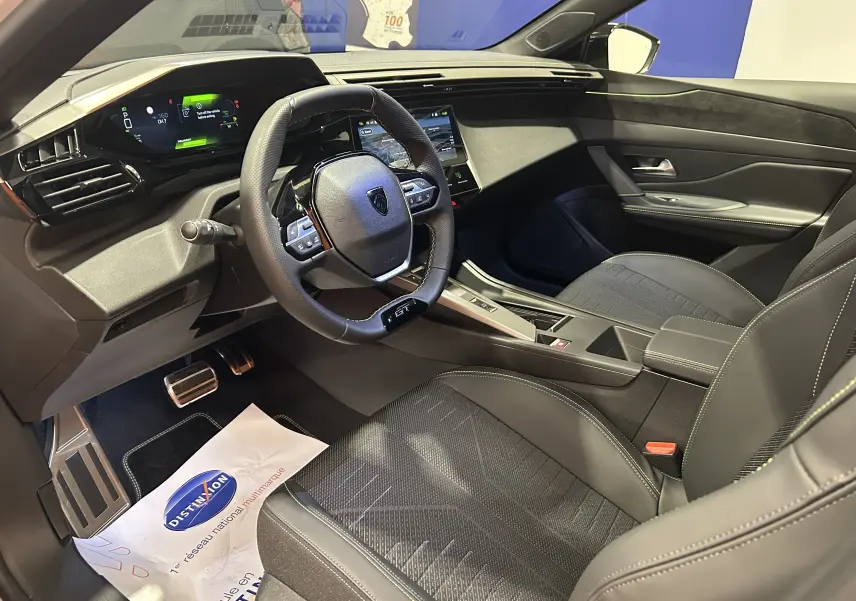 Vue intérieure côté conducteur de la Peugeot 308 HYBRID 145 GT avec tableau de bord numérique et volant compact cuir noir.