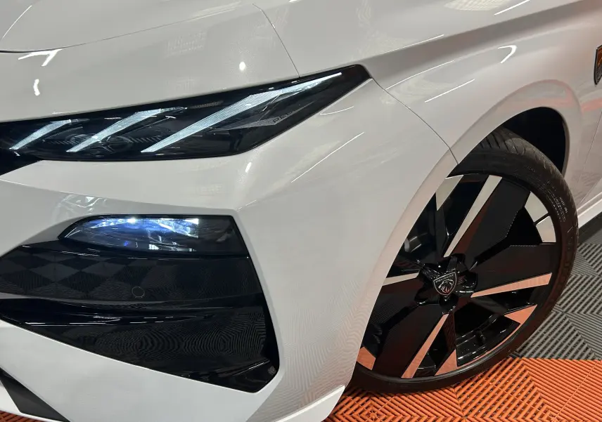 Gros plan sur l'avant droit blanc Okenite du Peugeot 308 III Ph.2 HYBRID 145 GT avec phare LED et jante noire bicolore.