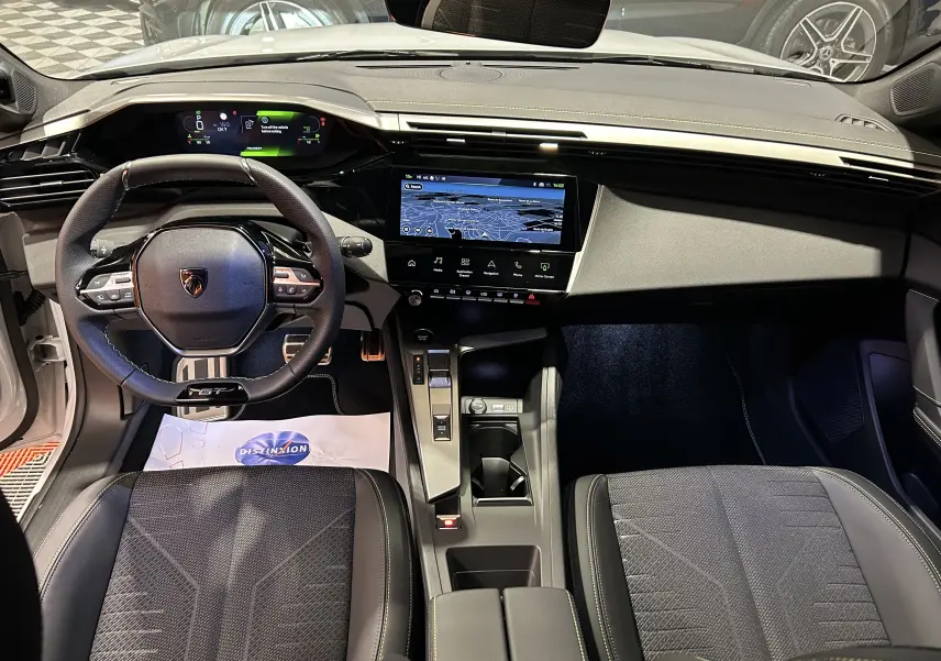 Vue intérieure frontale du poste de conduite de la Peugeot 308 HYBRID 145 GT, avec tableau de bord numérique et écran tactile GPS.