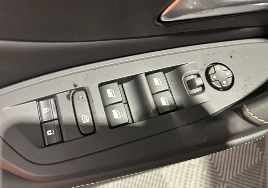 Gros plan sur les commandes de lève-vitres et rétroviseurs côté conducteur d'une Peugeot 308 blanche.