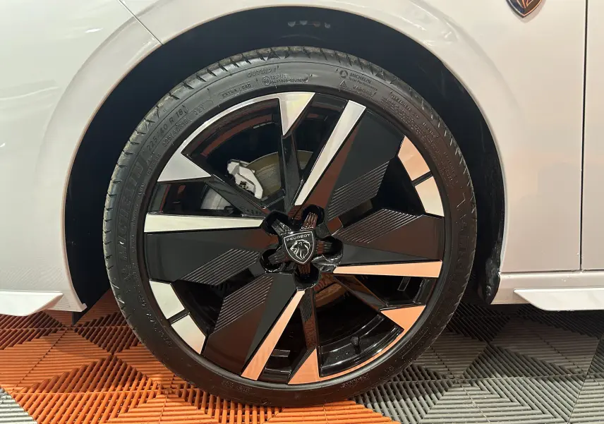 Gros plan sur la roue avant droite noire et argentée du Peugeot 308 blanc Okenite 2026, avec logo lion central.