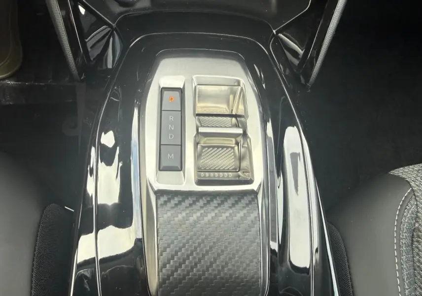 Vue rapprochée de la console centrale noire brillante avec sélecteur de vitesse électronique et accoudoir en carbone dans une Peugeot 208 gris.